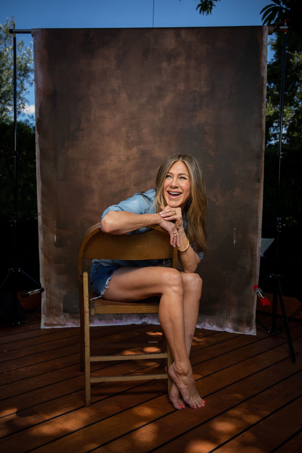  Jennifer Aniston sitting backward in a folding chair and smiling