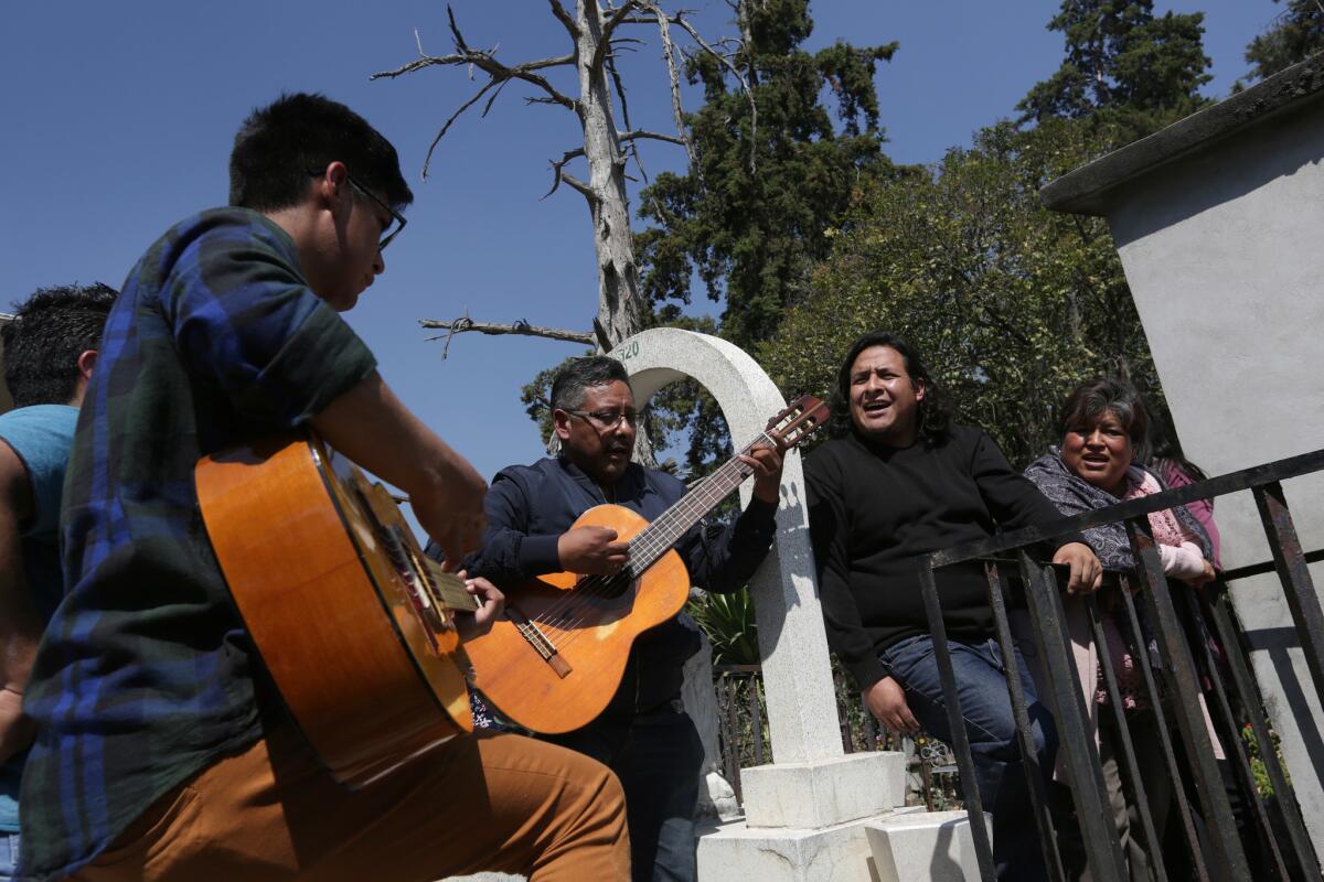 Edgar Hernandez Chavez, left, and Hugo Hernandez Chavez, second from right, play music and sing at their father’s grave with relatives Alvaro Chavez Vasquez and Angela Hernandez Sanchez. (Katie Falkenberg / Los Angeles Times)