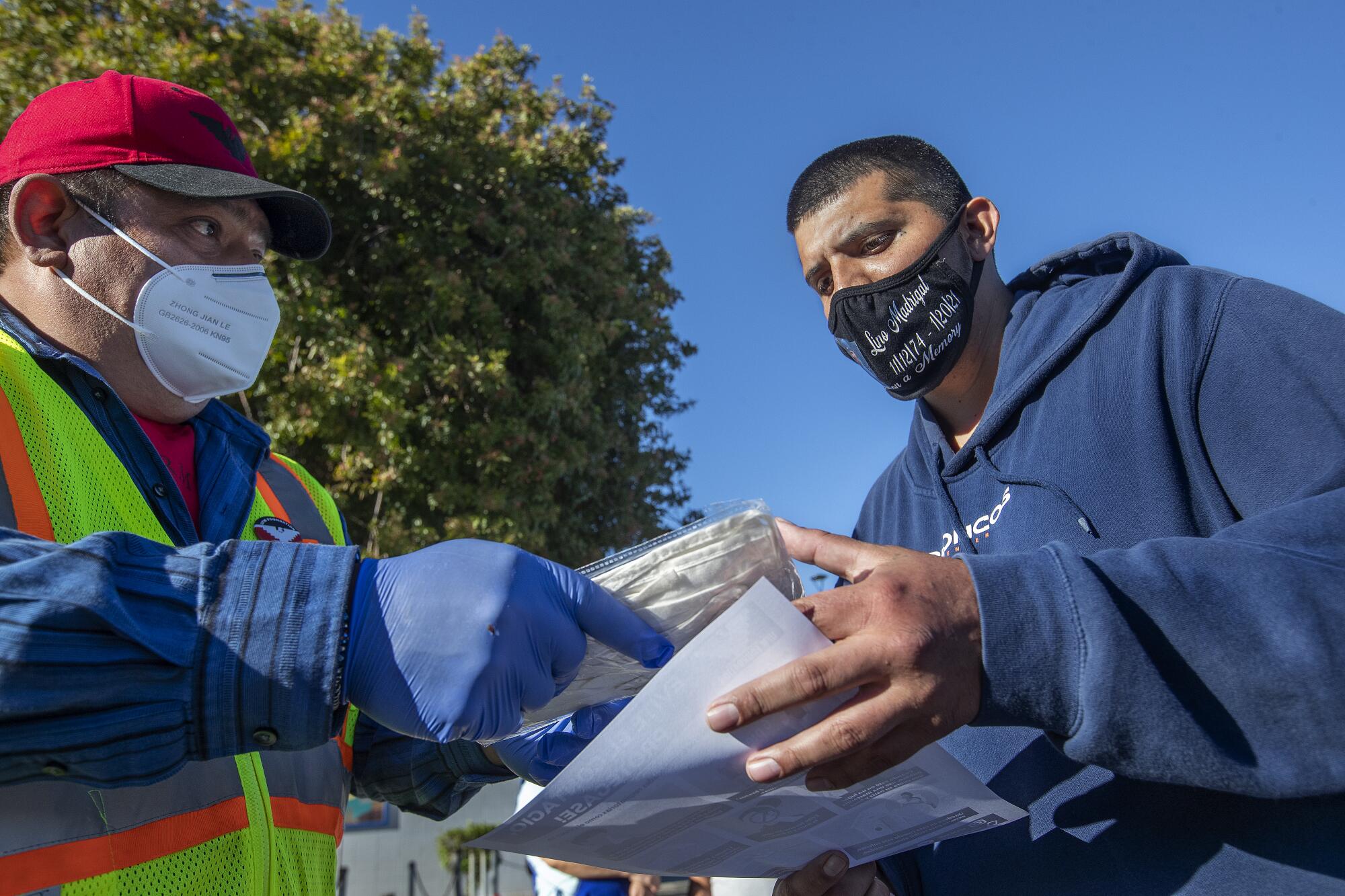 Salvador Villasenor, left, a volunteer with UFW, hands a packet containing cloth masks to Lompoc resident Richard Lopez.