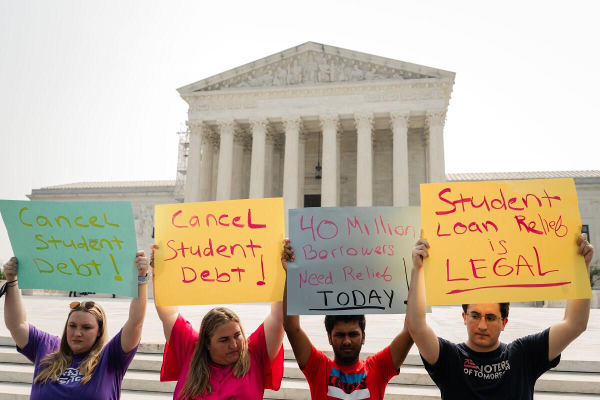 Four people stand in front of the Supreme Court building raising signs with messages such as "Student loan relief is legal."