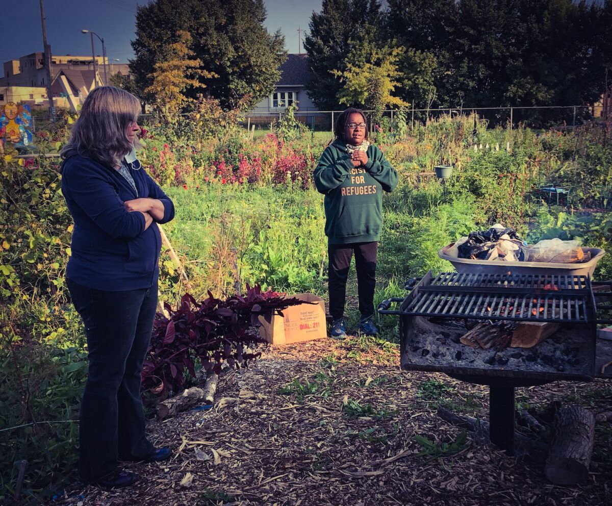 Venice Williams, right, stands and peaks in a community garden as another woman watches.
