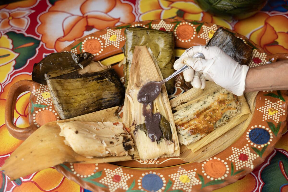 Mole tamales wrapped in banana leaves, rear; chicken, front left, bean tamale being covered with a bean sauce and chepil