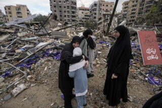 A woman hugs her crying daughter amid ruins