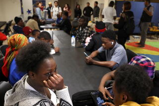 People sit facing others at tables pushed together, with other people standing in the background
