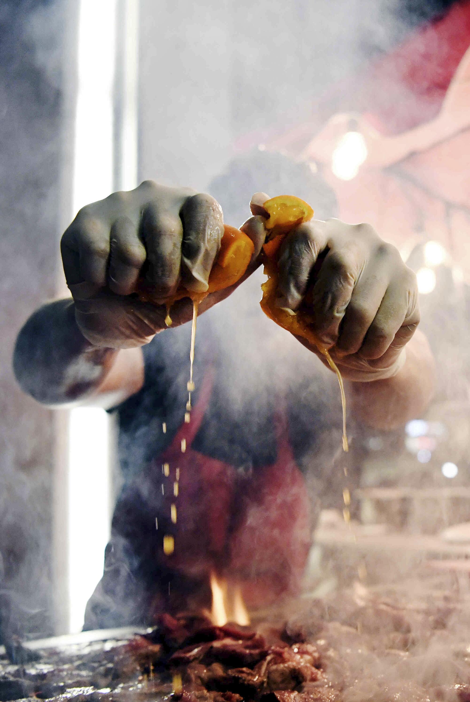  Jorge Alvarez squeezes liquid on cooking meat amid steam.