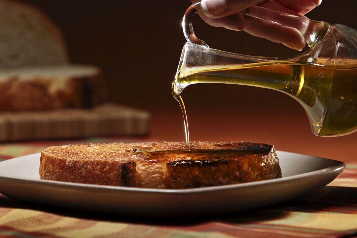 Drizzling extra virgin olive oil on a crusty country loaf of bread rubbed with fresh garlic to make a Bruschetta.