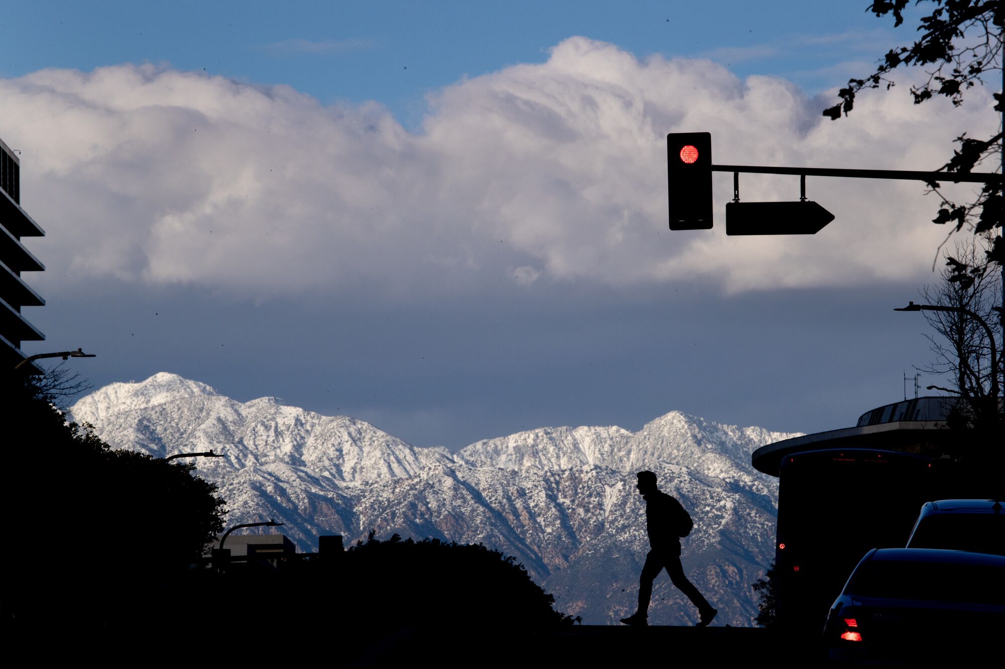 A pedestrian, crossing a street in downtown Los Angeles, is silhouetted against the snow-capped San Gabriel Mountains 