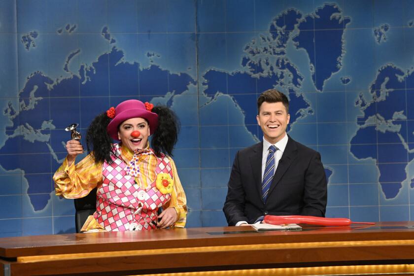 A woman in a clown costume and a man in a suit sitting behind a news desk
