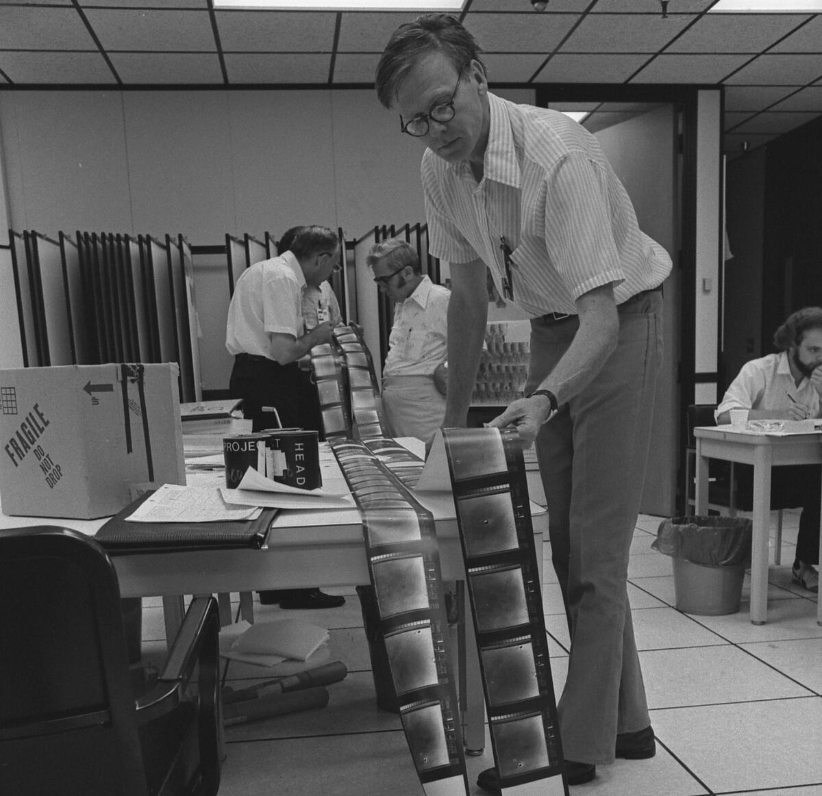 Rolls of film are spread out on a table as men with pens in their shirt pockets examine the images.