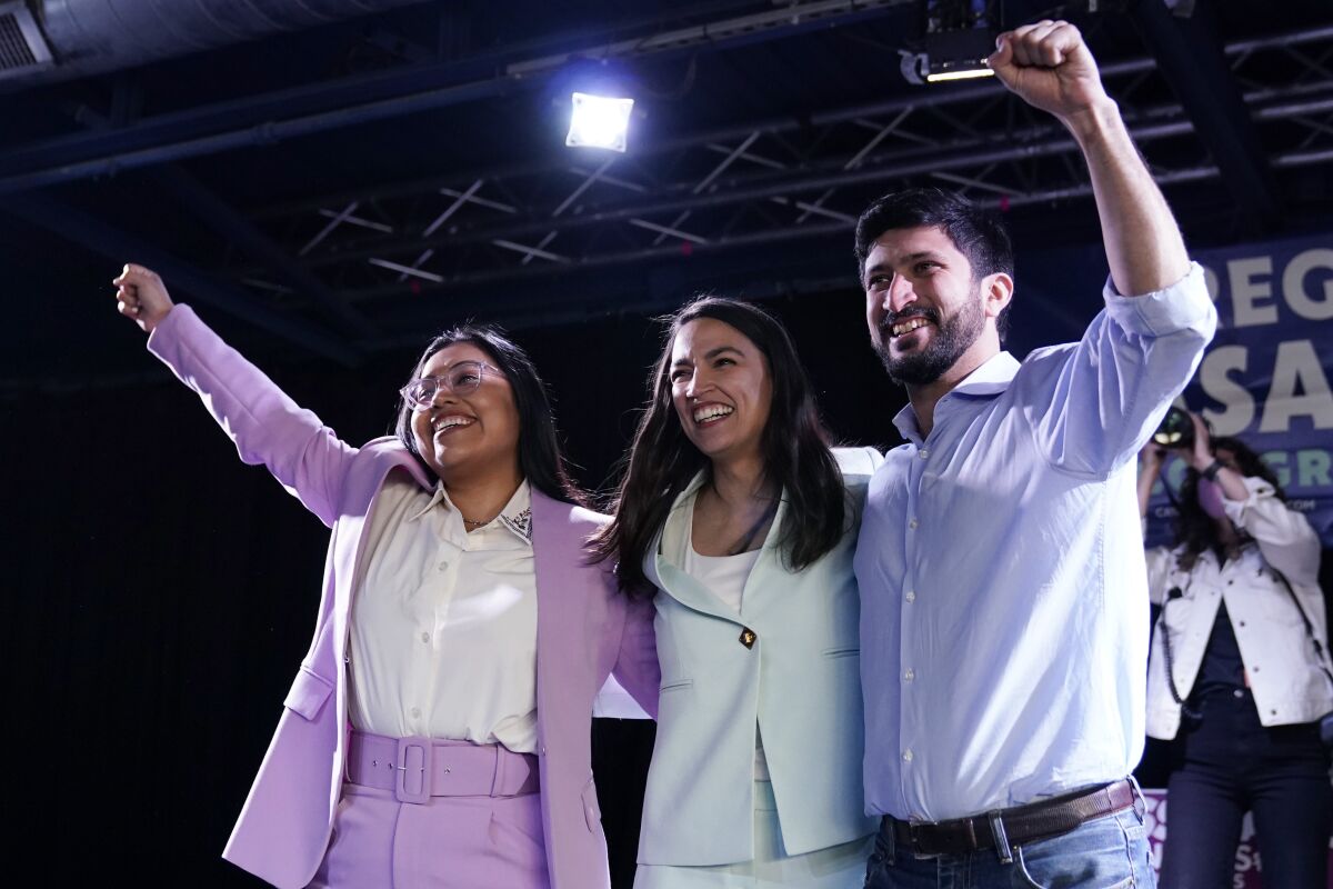 Alexandria Ocasio-Cortez beaming as she stands with her arms around a smiling woman and man with their fists in the air 