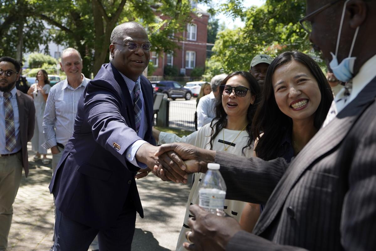 Michael Cox, left, who has been named as the next Boston police commissioner, shakes hands while greeting people as Boston Mayor Michelle Wu, right, looks on as they arrives at a news conference, Wednesday, July 13, 2022, in Boston's Roxbury neighborhood. Cox, who was beaten more than 25 years ago by colleagues who mistook him for a suspect in a fatal shooting, served in multiple roles with the Boston Police Department before becoming the police chief in Ann Arbor, Michigan, in 2019. (AP Photo/Steven Senne)