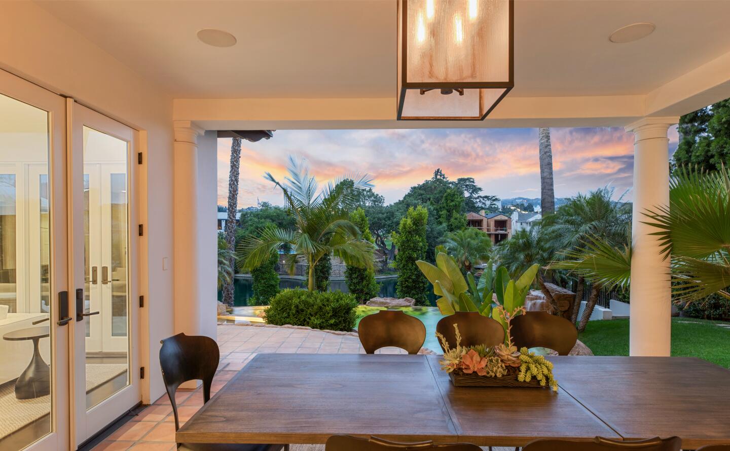 Covered patio with lighting a dining table and a view of greenery and the sky.