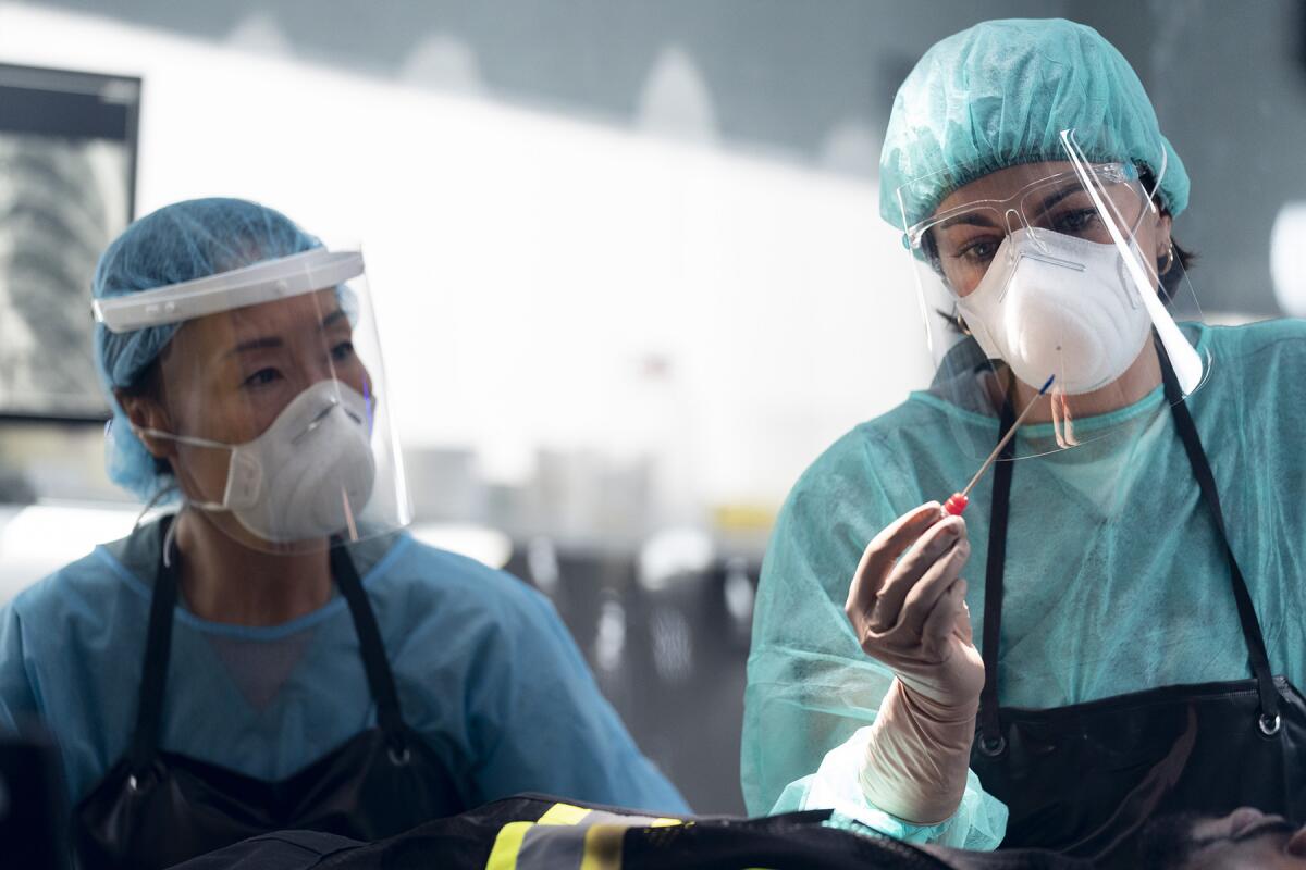 Two women wearing scrubs, face masks and shields examine an object.  