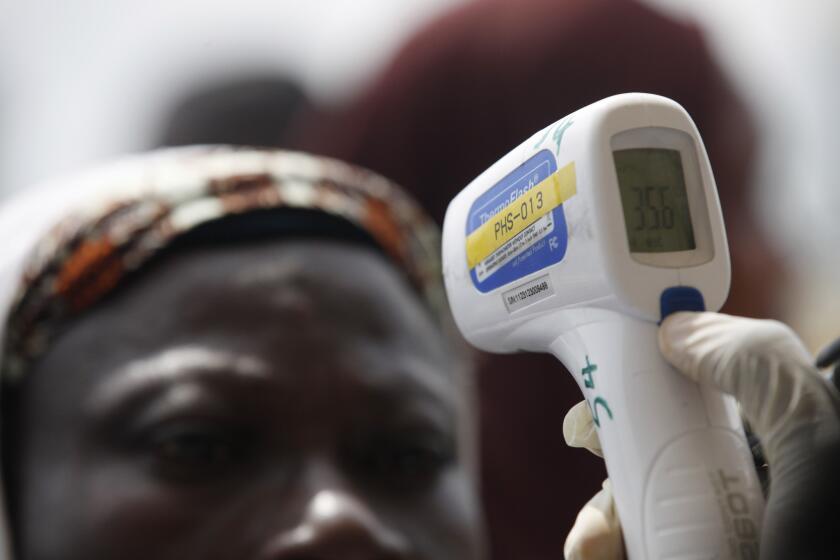 A port official at Murtala Muhammed International Airport in Lagos, Nigeria, takes a departing traveler's temperature as part of the screening for Ebola.
