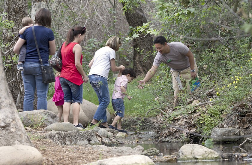 Naturalist Chhay Liv helps kids and parents across a small creek as they walk a trail at the Enviornmental Nature Center during a class on Wednesday.