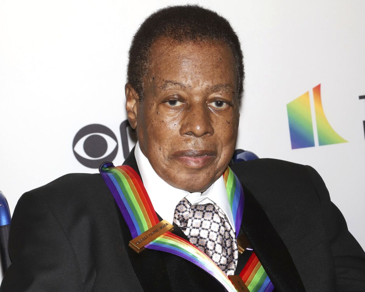 A man in a formal suit wears a colorful award around his neck.