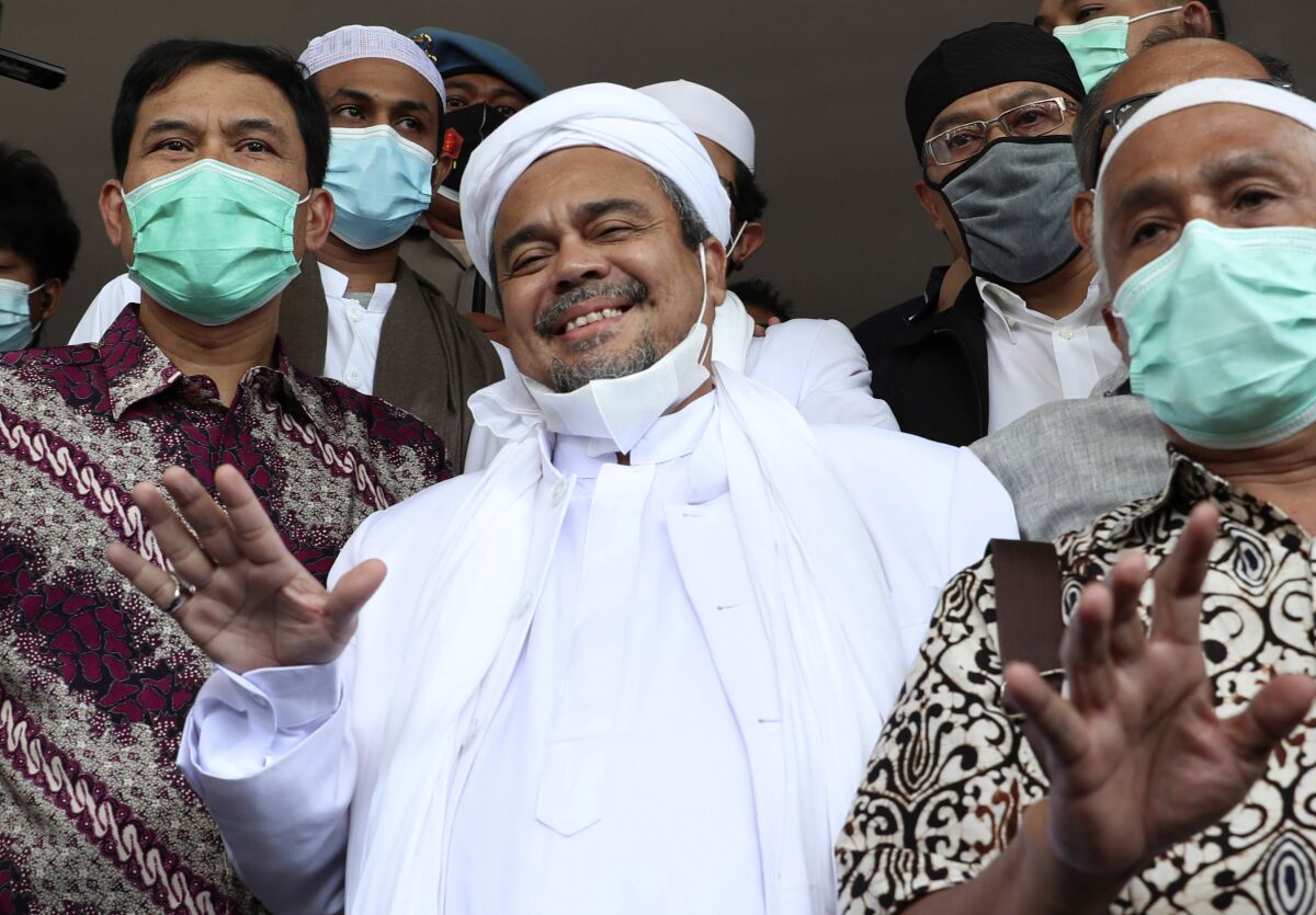 Indonesian Islamic cleric and the leader of Islamic Defenders Front Rizieq Shihab, center, gestures at reporters upon arrival at the regional police headquarters in Jakarta, Indonesia. Saturday, Dec. 12, 2020. The firebrand cleric turned himself in to the police after he was accused of inciting people to breach pandemic restrictions by holding events with large crowds. Shihab arrived at Jakarta police headquarters a day after police warned they would arrest him after he ignored several summonses. (AP Photo/Achmad Ibrahim)