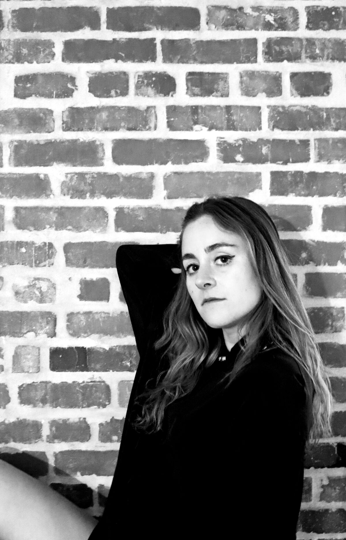 A woman poses in front of a brick wall.