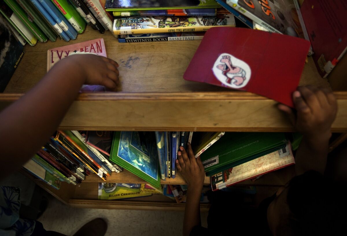 Children peruse a book cart filled with books in the library at San Pedro Elementary. For many low-income students throughout L.A. Unified, school is their main source for books and reading.