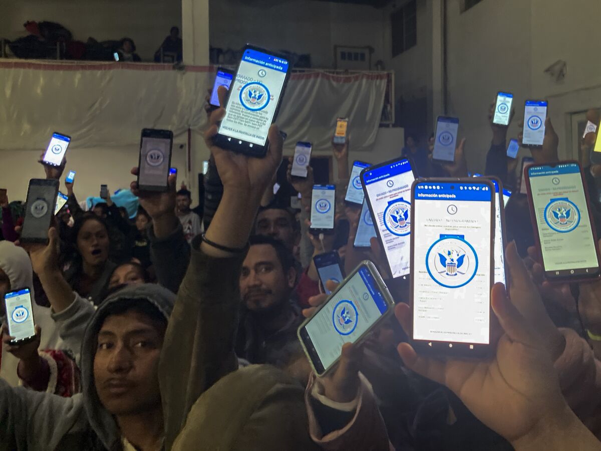 Decenas de migrantes muestran sus teléfonos mostrando en ellos la app CBPOne, en un albergue en Tijuana