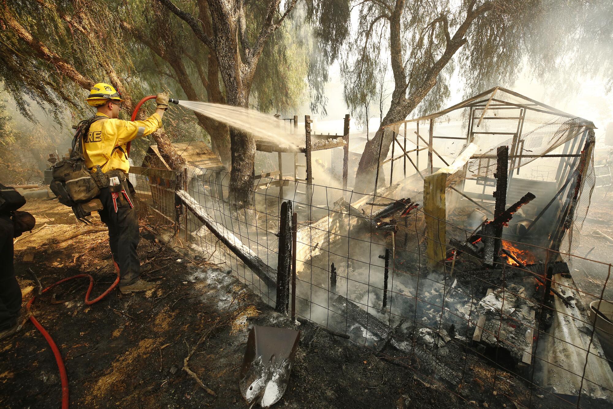 A firefighter uses a small hose to wet down the remnants of a burning animal pen