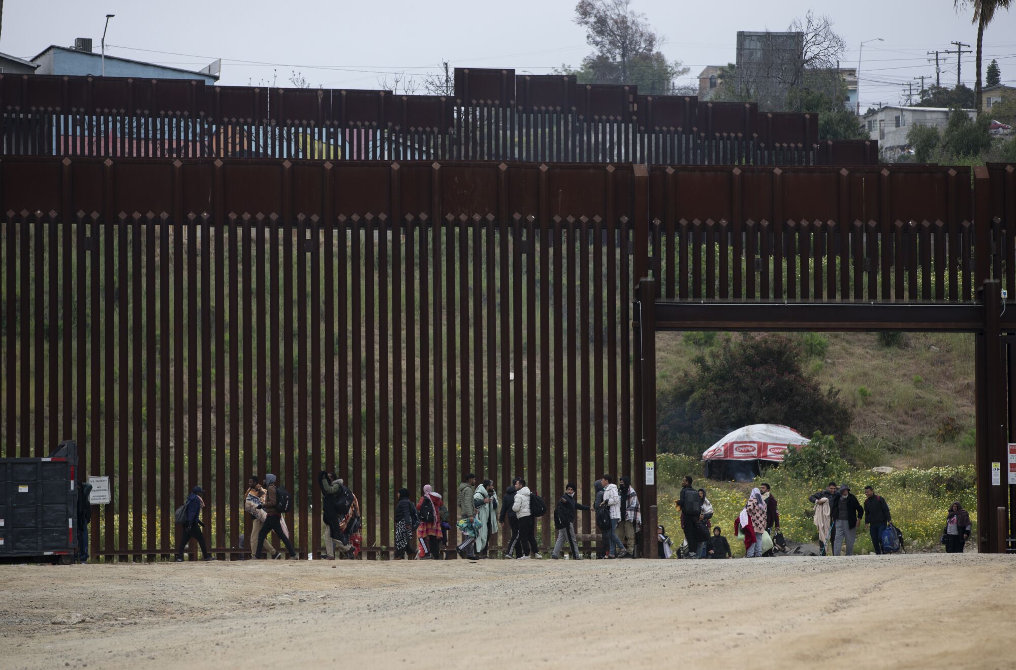 Dozens of asylum seeking migrants run out of an open gate before being stopped by U.S. Border Patrol agents