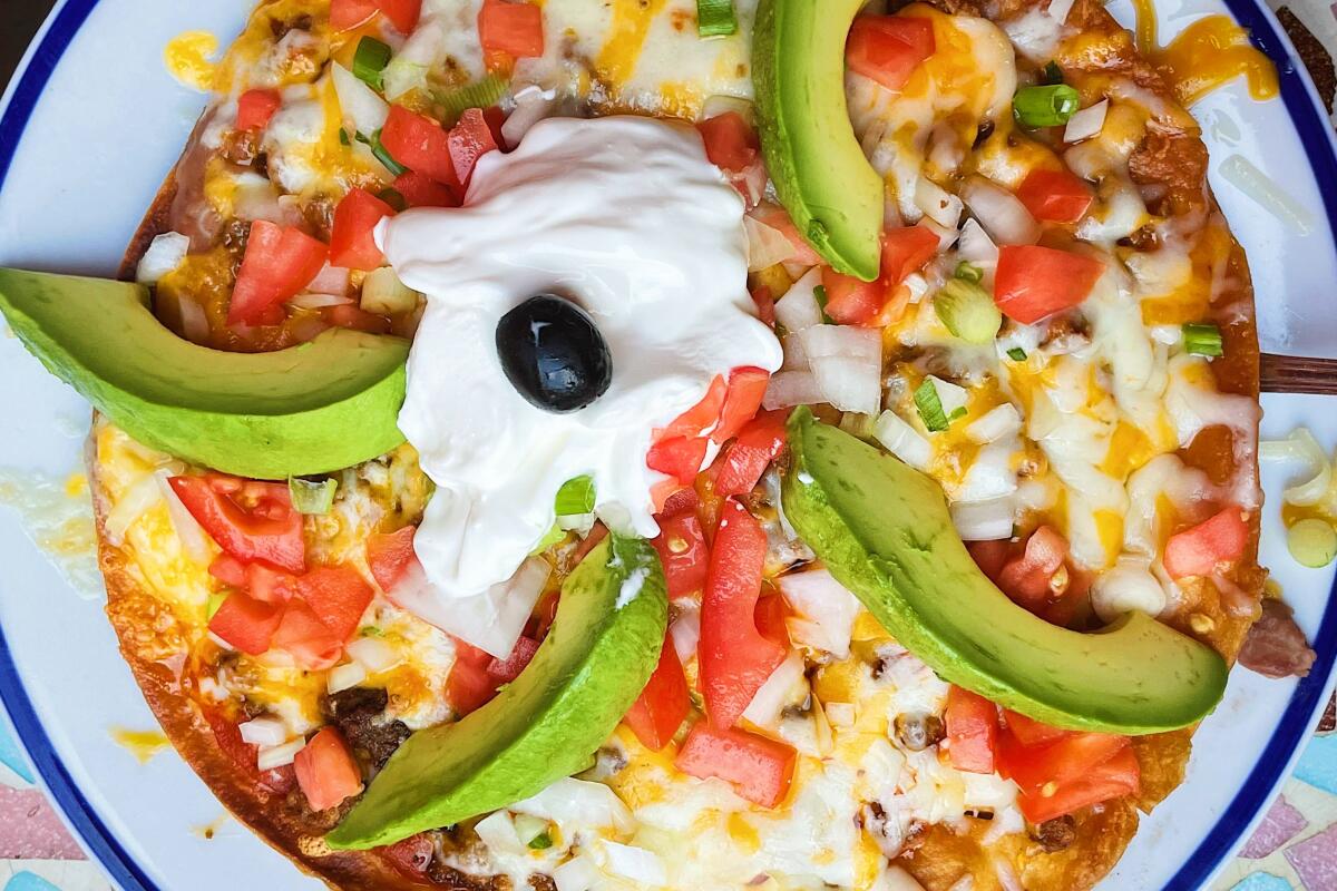 An overhead photo of the Mijares Mexican pizza, topped with avocado, sour cream, tomatoes, cheese, onions and a black olive.