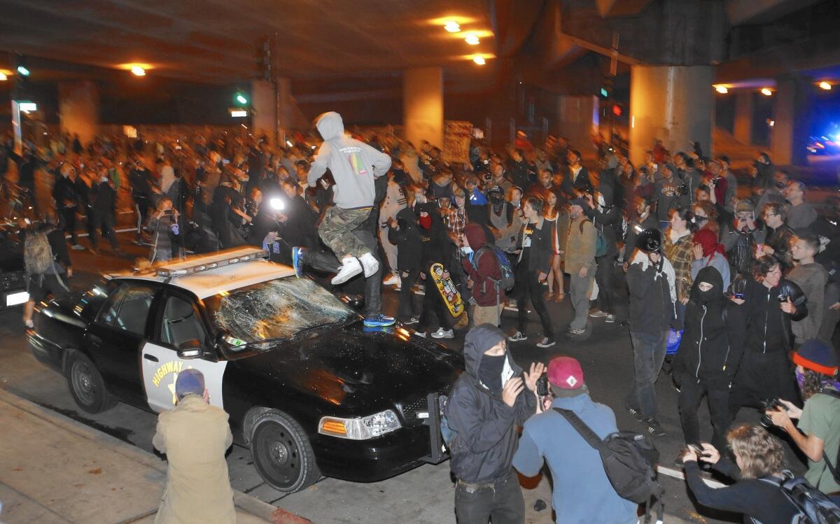 A man jumps on a vandalized California Highway Patrol squad car in Oakland on Sunday during another night of demonstrations.