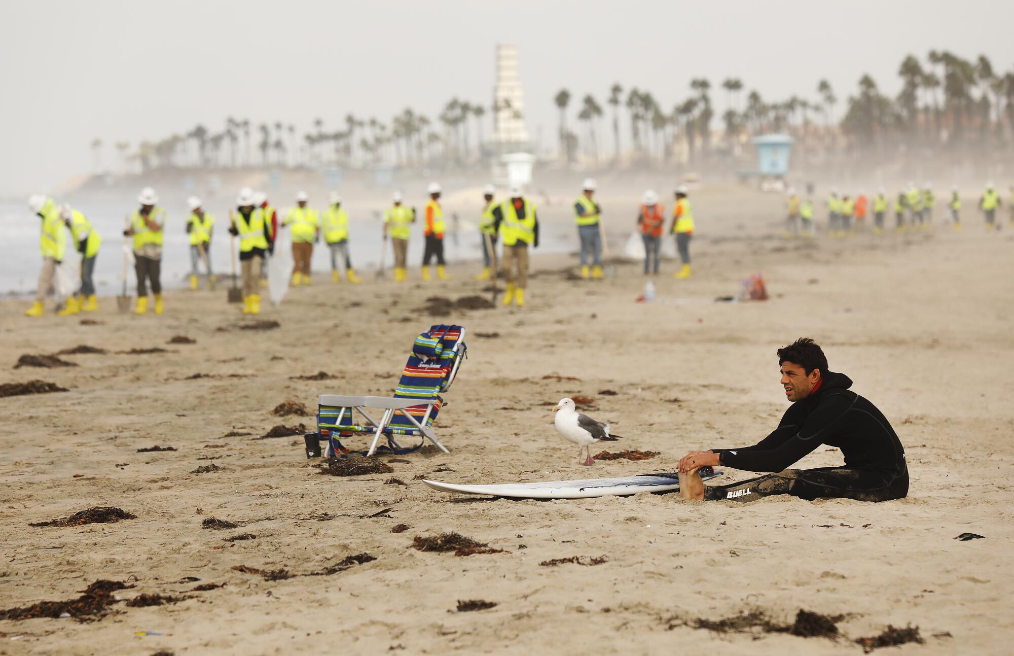 A surfer stretches with a cleanup crew in the background