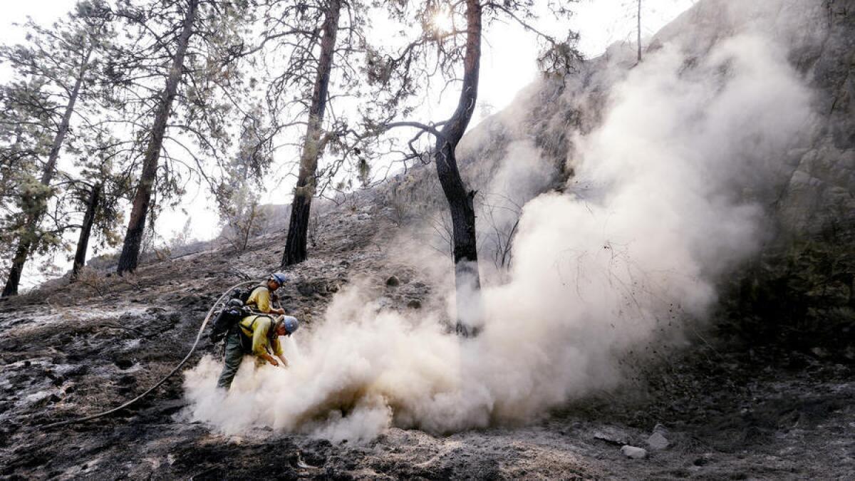 Estudiantes de bomberos de la Universidad de Alaska-Fairbanks, Preston Roberts y Ben Schrage, envían una nube de vapor mientras sofocan un punto caliente que quedó de un incendio forestal en Chelan, Washington.