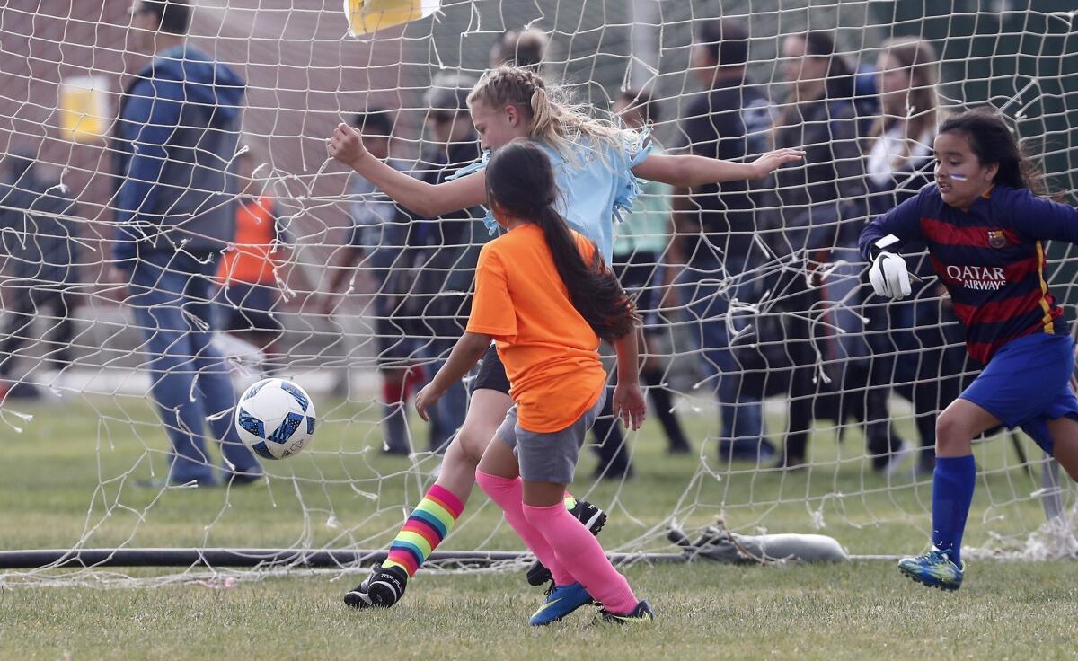 St. Joachim Catholic School's Ava Farrow, center, scores against Wilson's Emma Aguayo, left, and goalkeeper Emily Ebergenyi in a girls' third- and fourth-grade Bronze Division pool-play match at the Daily Pilot Cup on Friday at Costa Mesa High.