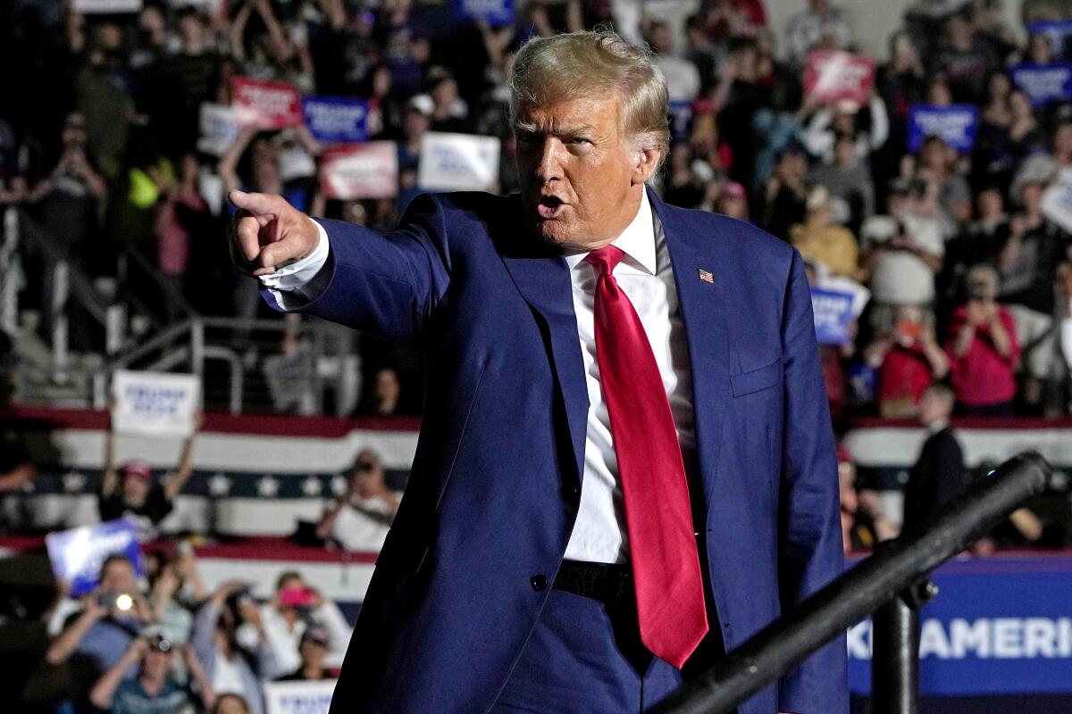 Donald Trump in a blue suit and red tie, pointing at a campaign rally.