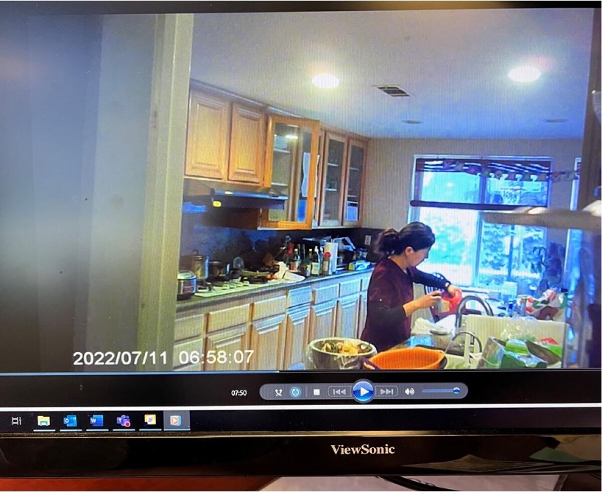 A woman in a kitchen, pouring from an orange container, in an image from a video marked 6:58 a.m. on July 11, 2022.