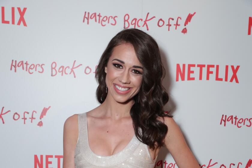 Colleen Ballinger is posing and smiling hand to her hip while wearing in a shiny, gray dress at a red carpet event
