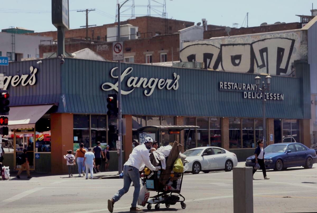 A man walks with his belongings in a shopping cart across the street from Langer's Deli near MacArthur Park on Aug. 21. 