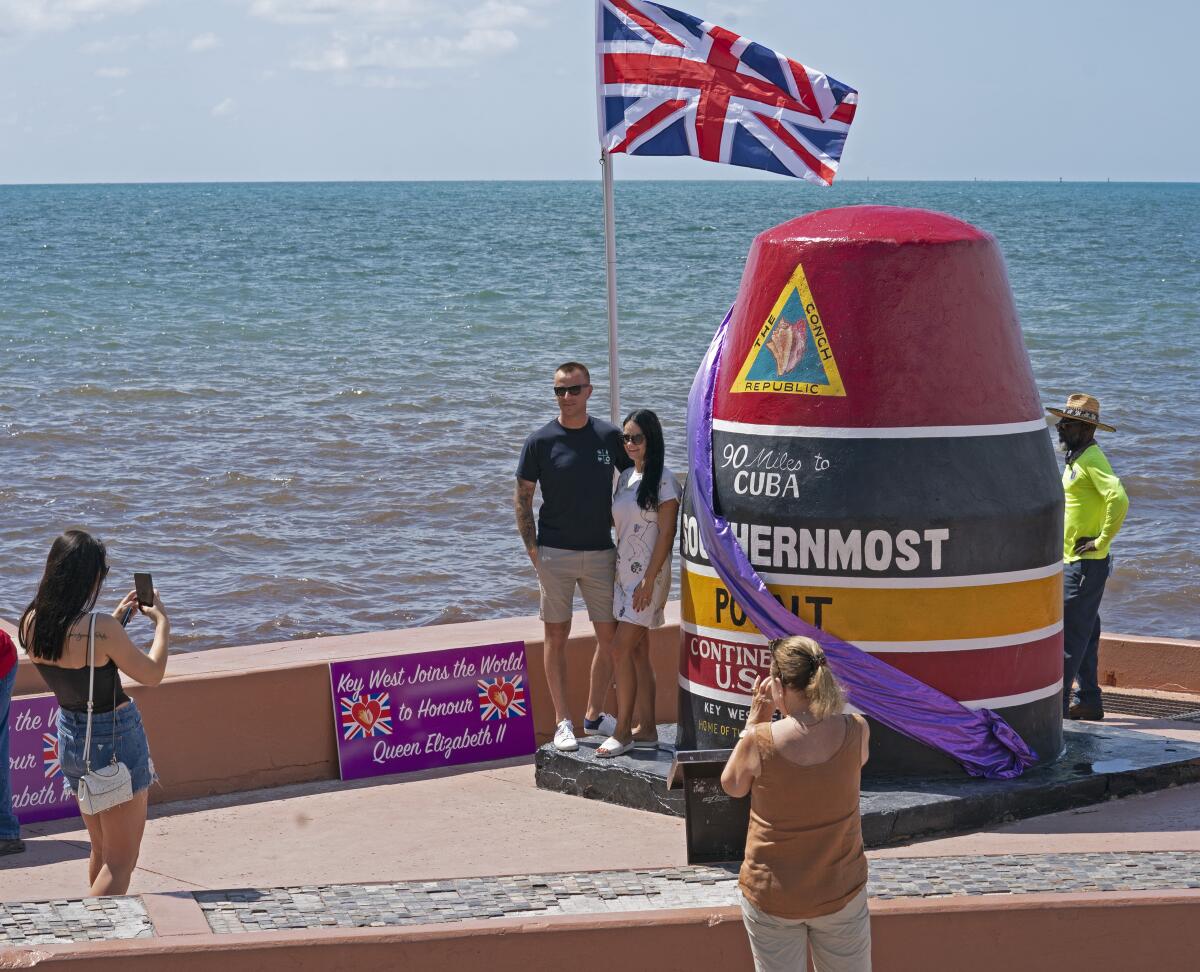 In this photo provided by the Florida Keys News Bureau, visitors are photographed next to the Southernmost Point marker that has been adorned with a purple sash to memorialize Queen Elizabeth II Friday, Sept. 16, 2022, in Key West, Fla. The Queen and Prince Philip visited the Florida Keys May 18, 1991, and toured historic Fort Jefferson in the Dry Tortugas. Key West's Southernmost Point marker is a Florida Keys icon designating the southernmost point of land in the continental United States. (Rob O'Neal/Florida Keys News Bureau via AP)
