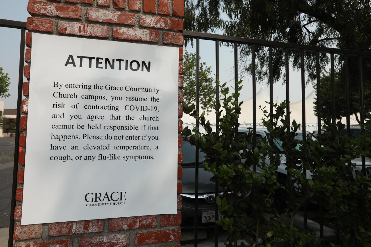 A sign on the back gate of the Grace Community Church states that all visitors assume the risk of contracting COVID-19.