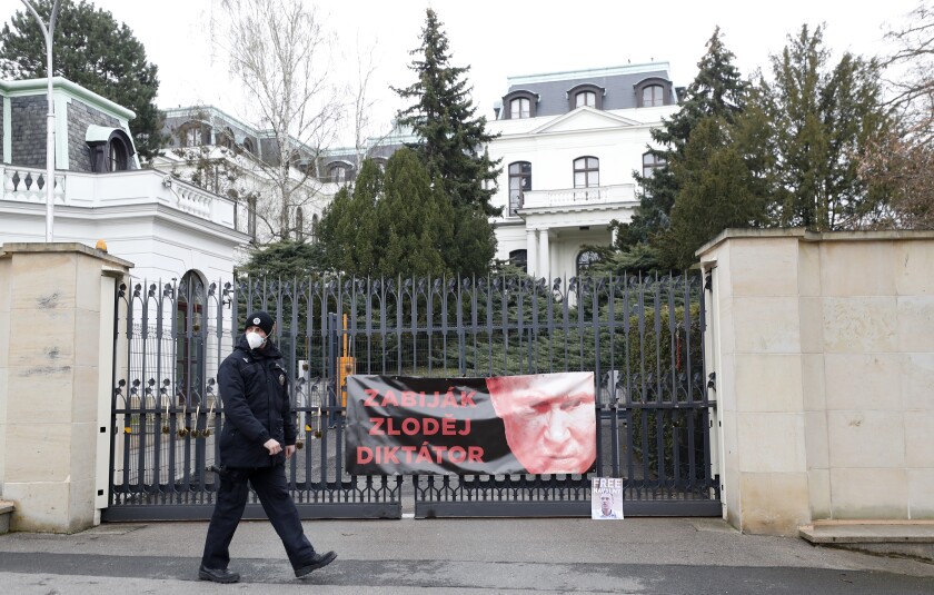 A policeman walks by a poster attached by protesters to a gate of the Russian embassy in Prague, Czech Republic, Friday, April 16, 2021. Czech Republic is expelling 18 diplomats identified as spies over a 2014 ammunition depot explosion. On Saturday, April 17, 2021, Prime Minister Andrej Babis said the Czech spy agencies provided clear evidence about the involvement of Russian military agents in the massive explosion that killed two people. The poster depicting Russian President Vladimir Putin reads: "Killer, Thief, Dictator". (AP Photo/Petr David Josek)