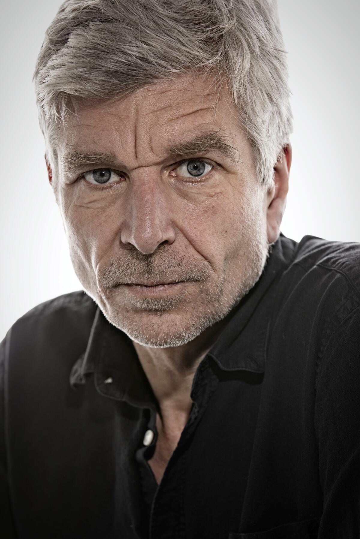 A gray-haired man looks directly into the camera