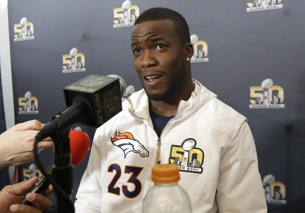 A man in a Denver Broncos Super Bowl sweatshirt with the No. 23 speaks in front of microphones