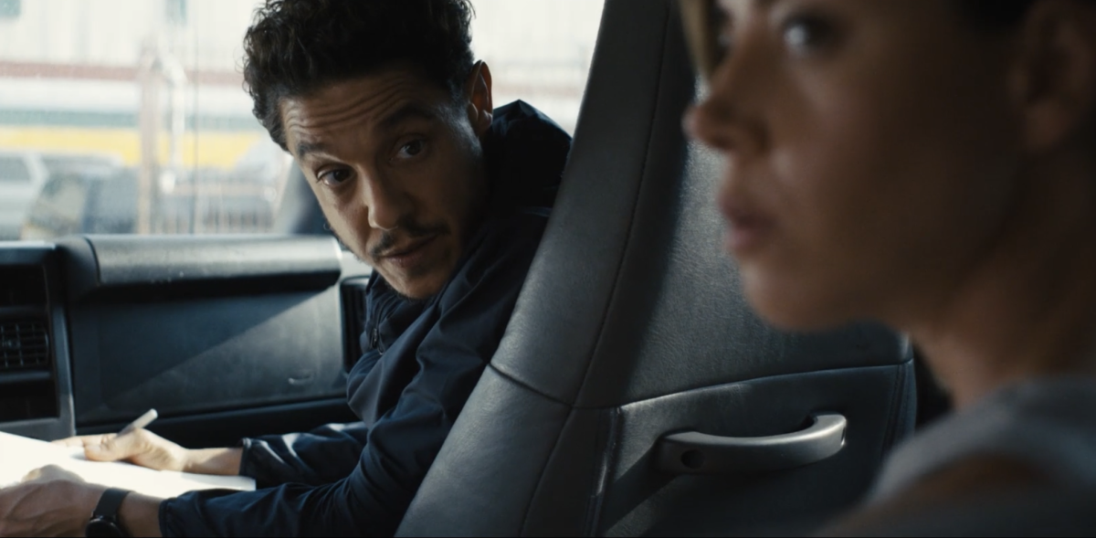 A man in the passenger seat of a car looks back at a woman in the back seat.