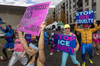 Protesters in 1980s style aerobic outfits hold signs reading "Stop ICE Cruelty."