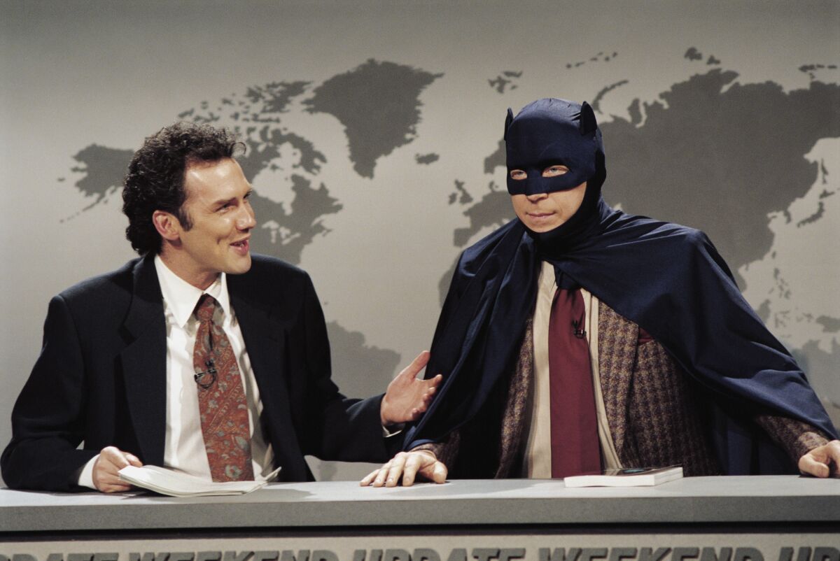 A man in a suit talks to a man in a Batman costume.