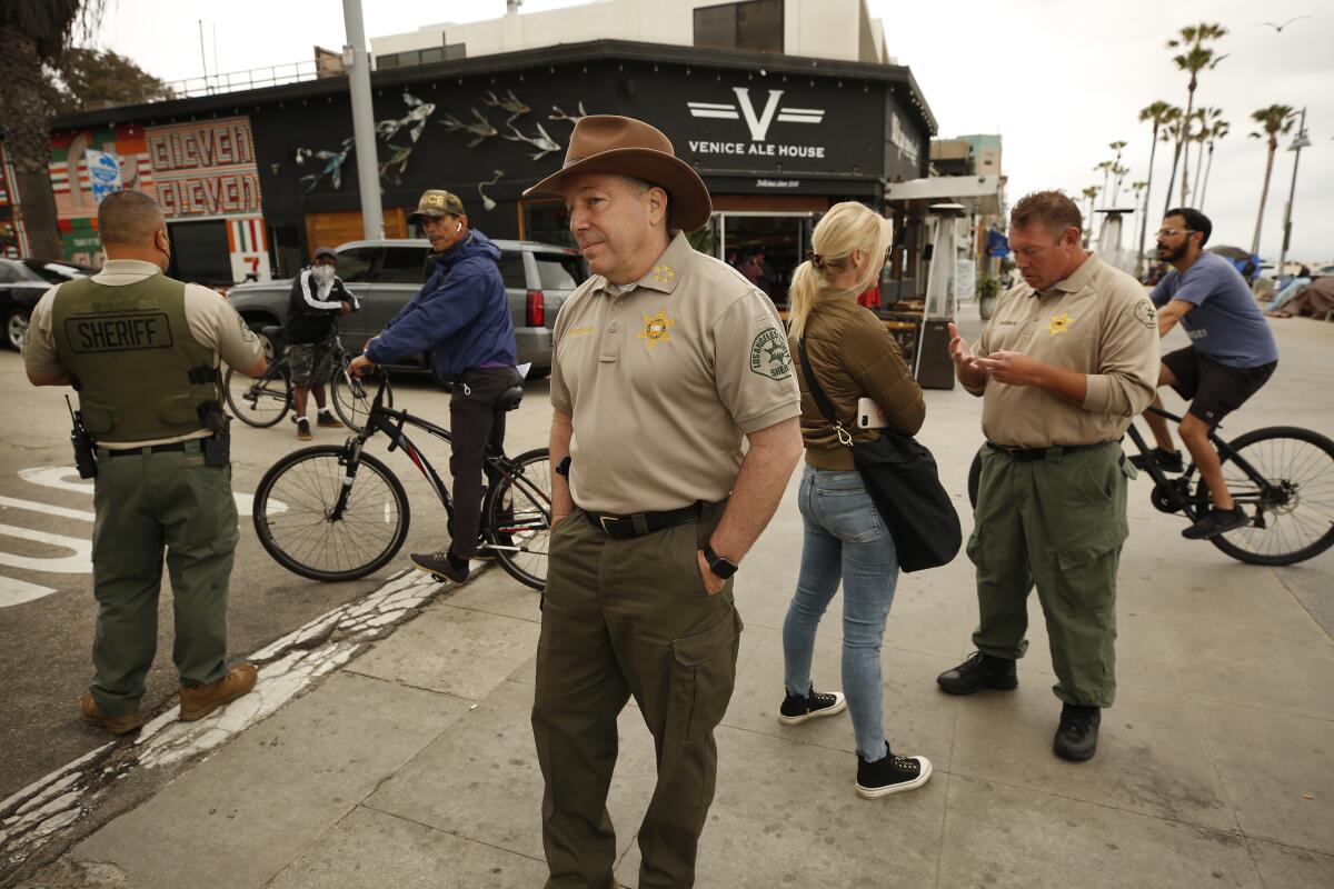 Sheriff Alex Villanueva stands on a sidewalk with cyclists and deputies behind him