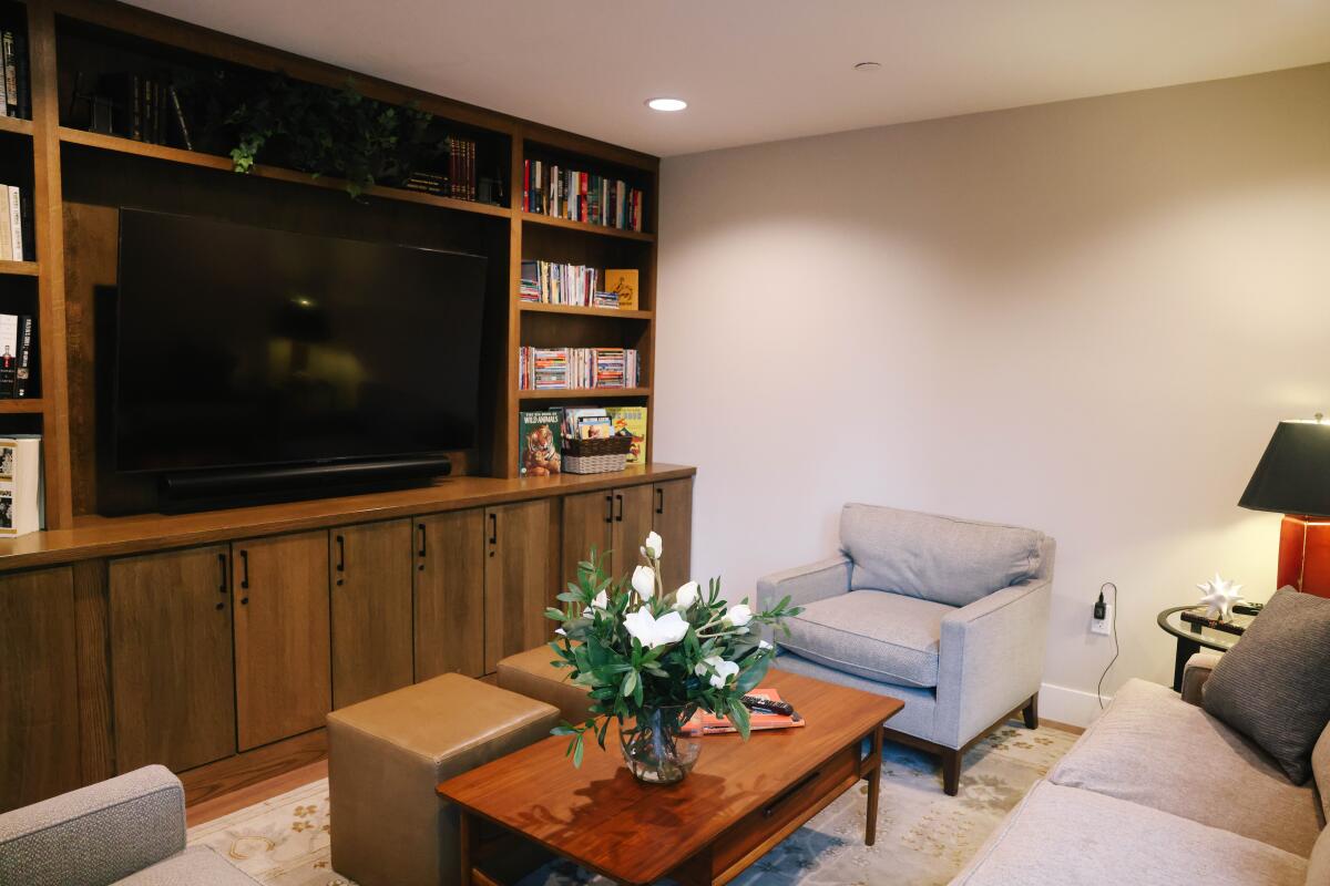 A room with a TV, bookshelves, chairs, a coffee table with a floral bouquet on top and a couch.