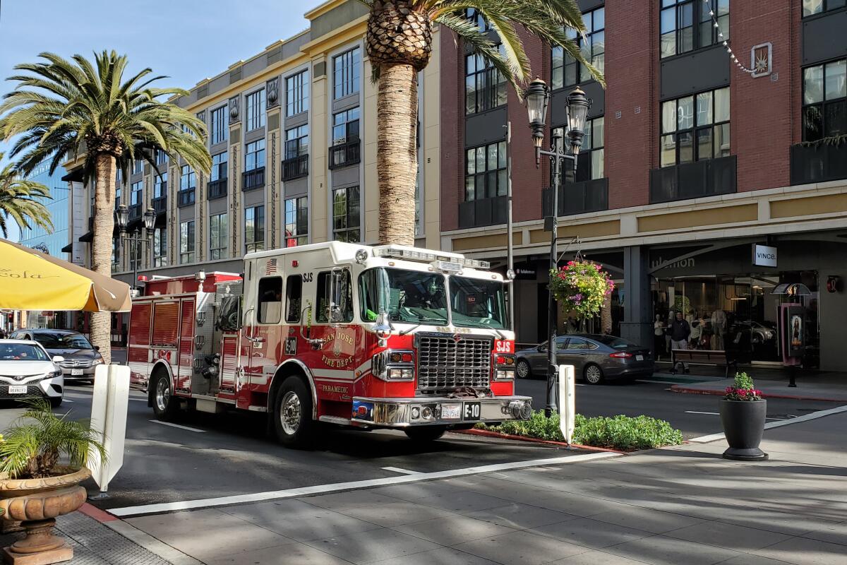 A firetruck driving past brick buildings and palm trees on a sunny city street 