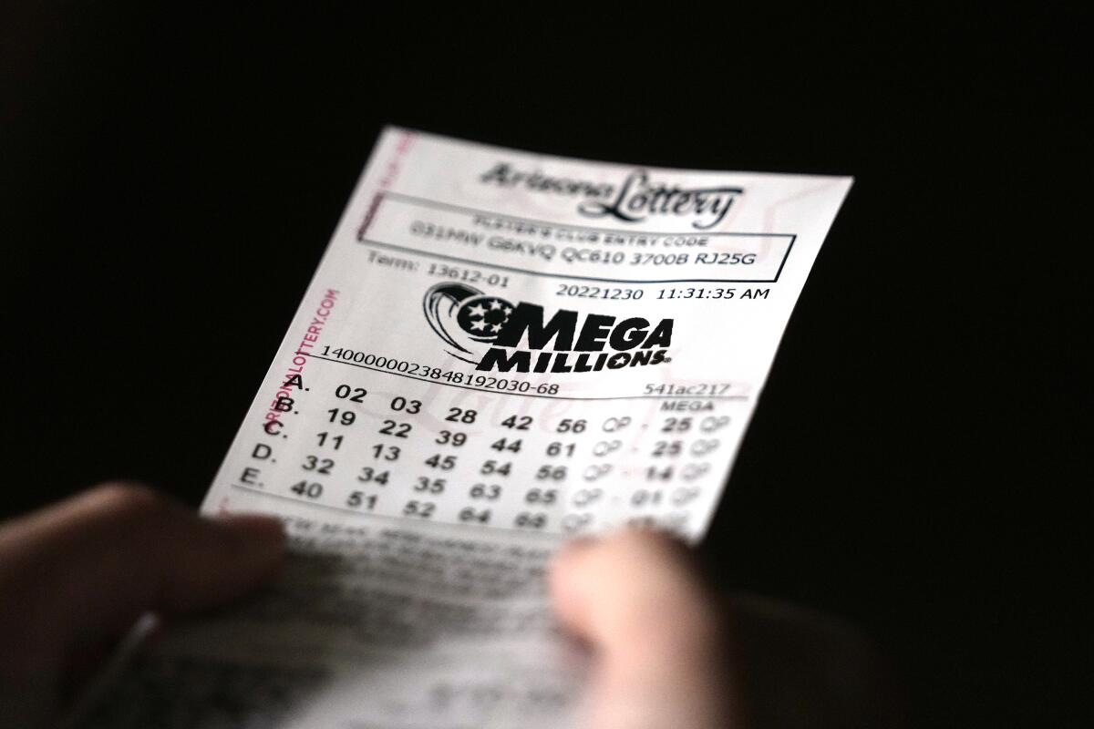 A very close-up view of a hand holding a  Mega Millions lottery ticket against a black backdrop.