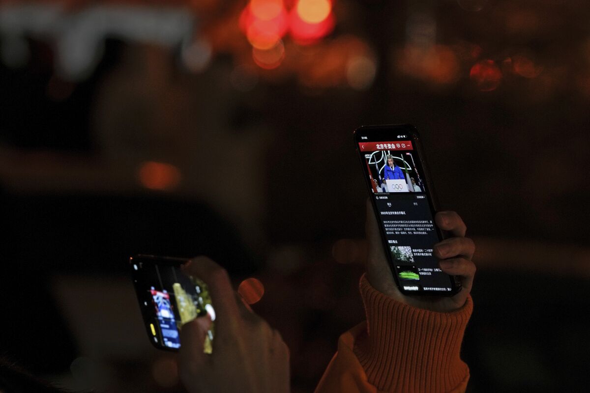 A resident uses her phone to film another smartphone showing President of the International Olympic Committee, Thomas Bach, speaking during the opening ceremony of the 2022 Winter Olympics, outside a residential block in Beijing on Feb. 4, 2022. The Winter Olympics are being held in Beijing, but most of the population is shut out because of coronavirus restrictions. The lack of interaction with visiting foreign athletes and spectators has intensified the sense that the Games are taking place several degrees removed from the daily life of the city and the nation. (AP Photo/Andy Wong)