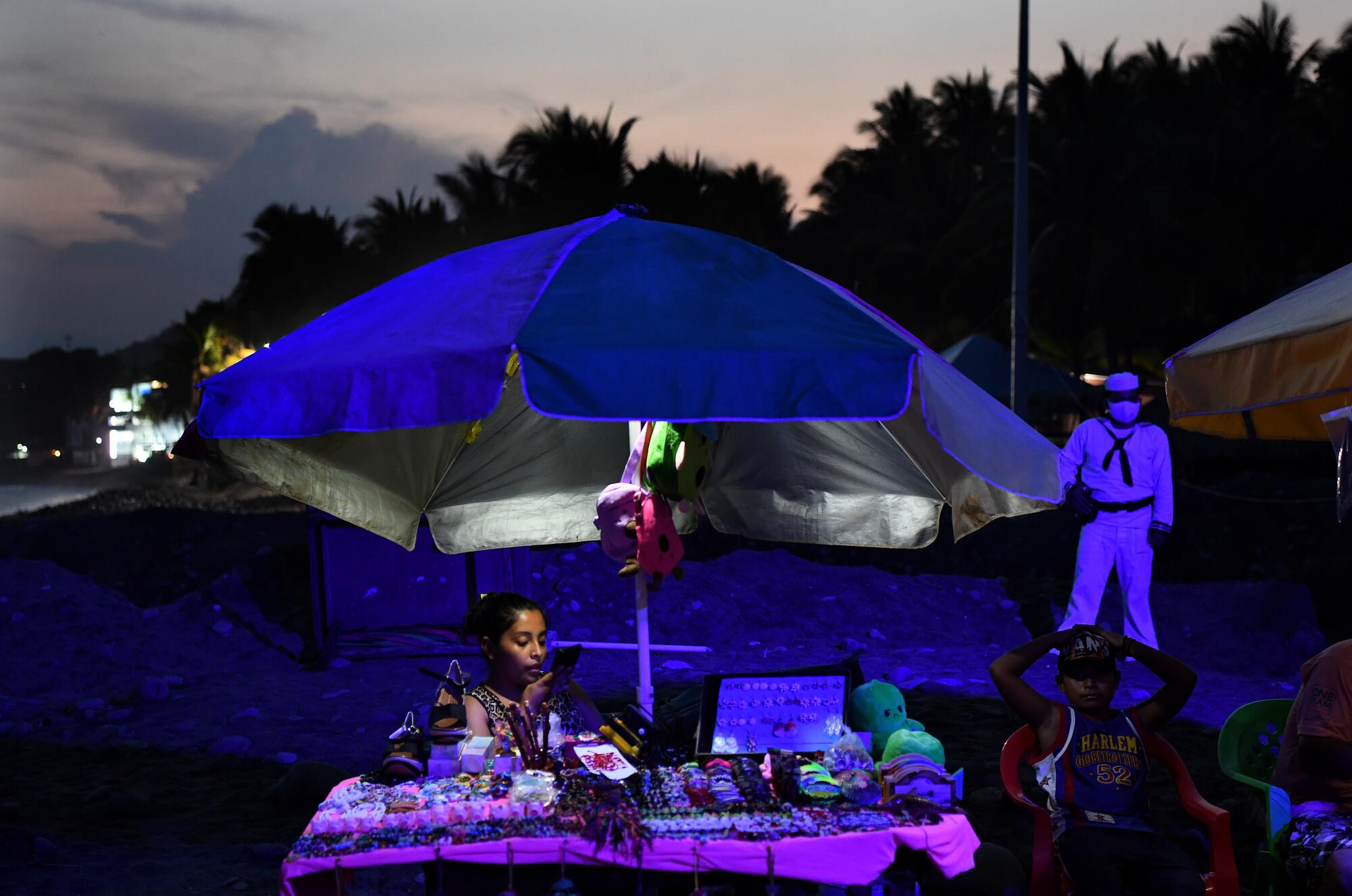 Street vendors sell goods on the beach as security looks on.