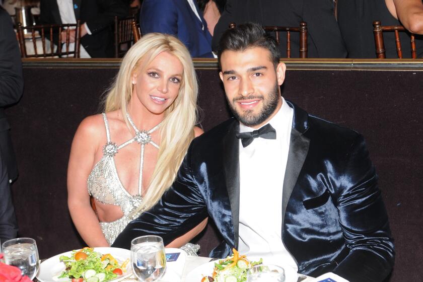 Britney Spears, wearing a silver dress, is sitting at a dinner table with Sam Asghari in a blue velvet suit